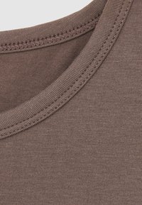 Gros plan sur un tissu marron avec une couture renforcée au niveau de l'encolure ronde sur un vêtement en coton.