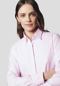 Jasnoróżowa koszula zapinana na guziki z usztywnionym kołnierzykiem i długimi rękawami. Posiada subtelny wzór teksturowy oraz mały detal z logo na mankiecie.