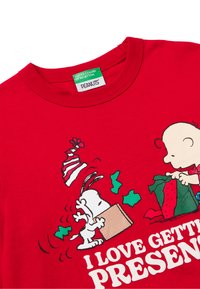 Camiseta roja de algodón con un gráfico de Snoopy y un niño, con el texto "ME ENCANTA RECIBIR REGALOS" en blanco. La etiqueta muestra el nombre de la marca.