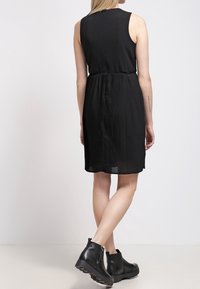 Černé bezramenné šaty s plisovanou sukní, se zapínáním na zip na zádech. V kombinaci s černými kotníkovými botami a hladkou texturou.