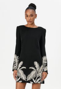 Black long-sleeve dress featuring intricate silver palm leaf embroidery at the hem. Smooth fabric with a boat neckline and structured shoulders.