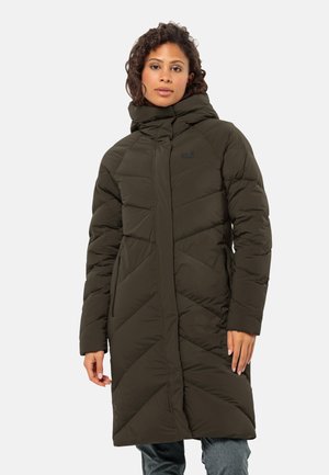 Woman wearing a dark green padded long winter coat with quilted diagonal stitching and a high collar.