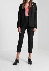 Svart kavaj med smalrand och matchande croppade byxor, kombinerat med en rosa t-shirt med röd text. Svarta loafers avslutar outfiten.