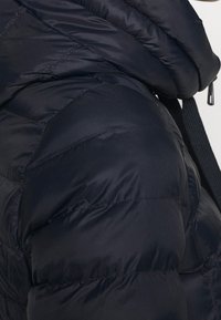 Giacca a vento blu navy con design trapuntato, caratterizzata da un collo alto e una cerniera, che mostra una texture liscia e lucida e un'imbottitura strutturata.