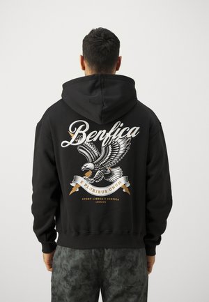 Sudadera negra con un gran gráfico de un águila y texto "Benfica" en blanco y dorado. Tejido suave, bolsillo frontal y capucha con cordón ajustable.