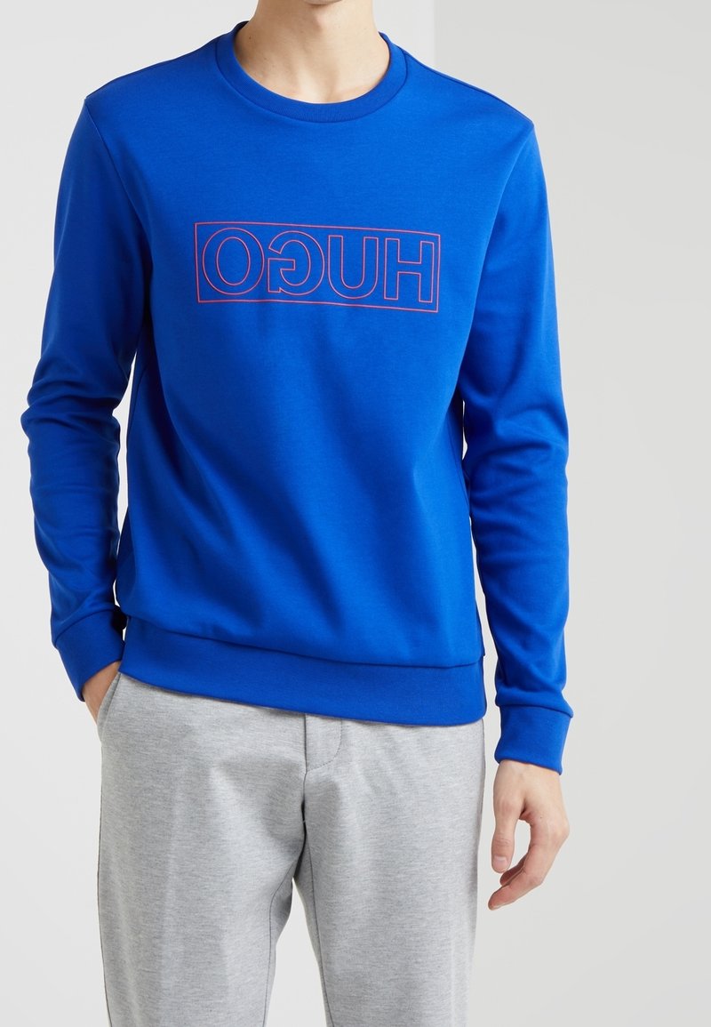 Felpa blu con maniche lunghe, polsini e scollatura a costine. Presenta un logo a quadrato rosso con il testo "HUGO" in lettere maiuscole.