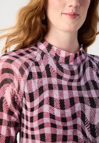 Langsleeve top met een roze en zwart geblokt patroon en een gestructureerde afwerking. Hoge halslijn en raglanmouwen.