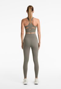 Ensemble de sport vert olive comprenant un haut court avec un design de découpe unique au dos et un legging taille haute avec une silhouette épurée.
