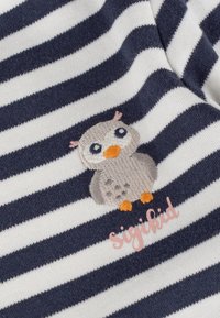 Navy und weiß gestrefter Stoff mit gestickter grauer Eule mit orangefarbenem Schnabel und Füßen sowie pinkem "Sigikid"-Text darunter.