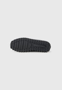 Black rubber shoe sole with thick tread pattern, featuring raised grooves and circular accents for grip. Smooth central section.
