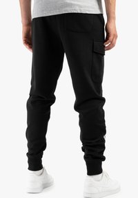 Svarta sweatpants i mjukt tyg, med en cargo-ficka på höger lår och ribbade muddar, i kombination med vita sneakers.