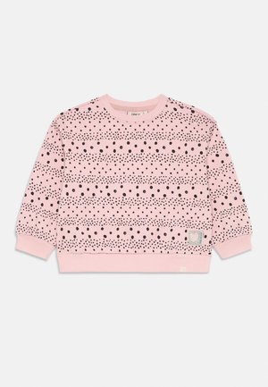 Rosa genser med lange ermer med svart spredt og stripet polkaprikkmønster, ribbestrikkede mansjetter og kant, og en liten hvit lapp på frontkanten.