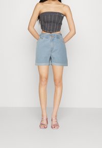Pantalones cortos de denim de color azul claro con dobladillos enrollados, con una cintura alta y un cierre de un solo botón. Combinados con una camiseta gris ajustada y sandalias rosas.