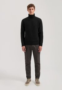 Schwarzer Rollkragenpullover mit geripptem Kragen und Saum, aus strukturiertem Strickstoff gefertigt. Kombiniert mit dunklen Hosen und grauen Sneakers.