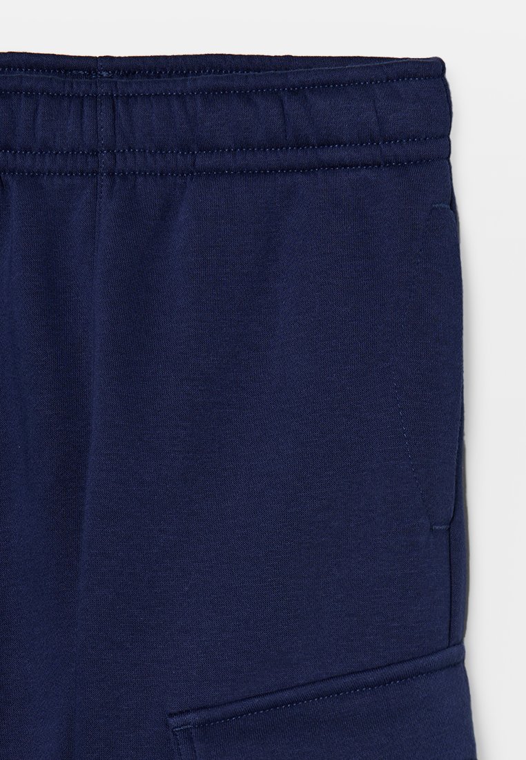 Dunkelblaue Sweatpants mit elastischem Bund, seitlicher Tasche und weichem, strukturiertem Stoff. Genähte Nähte entlang des Bundes und der Taschenkante.