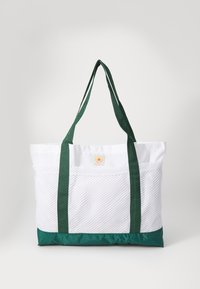 Sac fourre-tout avec un corps en maille blanche, un fond en nylon vert et des poignées. Affiche un logo circulaire sur le devant. Conception spacieuse et légère.
