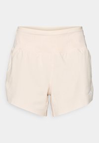 Shorts de sport beige clair avec une taille haute, fabriqués en tissu doux, présentant un détail de logo discret sur la partie inférieure de la jambe droite.