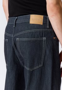 Σκούρα τζιν denim με αντιθετική ραφή, δερμάτινη ετικέτα «WEEKDAY» στη μέση και δύο πίσω τσέπες με λοξές ραφές.