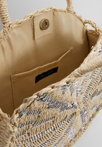 Woven straw bag with silver accents and a beige fabric interior. Features a secure snap closure and inner pocket.