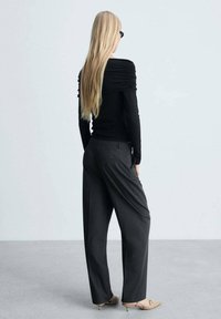 Top negru cu detaliu strâns pe umăr, asortat cu pantaloni gri largi și balerini bej, văzuți din spate.