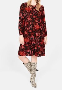 Robe noire avec motif floral rouge, manches longues et ourlet en dégradé ; assortie à des bottes jusqu'aux genoux en imprimé serpent en beige et noir.
