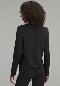 Top lungo nero a maniche lunghe realizzato in tessuto morbido. Presenta uno scollo a barca, una vestibilità comoda e dettagli di cucitura sottili sul retro.