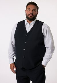Granatowa kamizelka o dopasowanym kroju, z pięcioma czarnymi guzikami i dwiema kieszeniami z boku, zestawiona z białą koszulą.