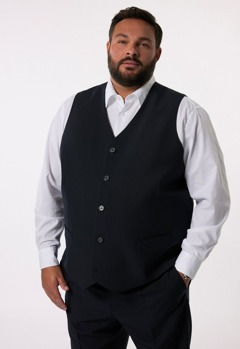Granatowa kamizelka o dopasowanym kroju, z pięcioma czarnymi guzikami i dwiema kieszeniami z boku, zestawiona z białą koszulą.