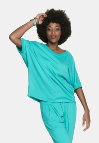 Turkusowa, luźna bluzka z krótkimi rękawami i okrągłym dekoltem, w zestawie z dopasowanymi spodniami. Gładka tekstura, casualowy design.
