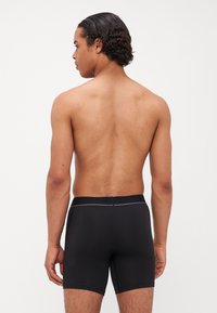 Boxer shorts pretos com um cós texturizado, revelando um design liso e ajustado. O tecido parece leve e elástico.