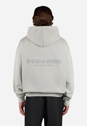 Light gray hoodie with a large back print reading "PEGADOR" and "CERTIFIED AUTHENTIC STREETWEAR." Loose fit with ribbed cuffs.