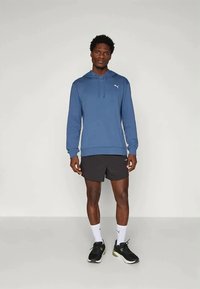 Blå hettegenser med snor, frontlomme og hvit logo. Brukt med svarte shorts og svarte treningssko.