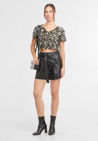 Krátký top s leopardím vzorem a krátkým rukávem, spárovaný s černými vysokým pasem šortkami z umělé kůže a kotníkovými botami. Krátký detail s uvázaným pásem.