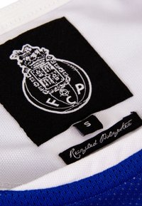 Blauw-wit sporttricot met een mesh-textuur. Heeft een zwart label met het witte logo "FCP" en een waslabel dat gerecycled polyester aangeeft, maat S.