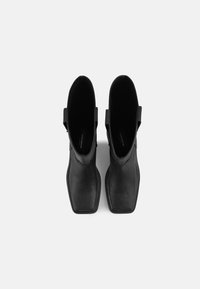 Botas de cuero negro a la altura del tobillo con punta cuadrada, diseño minimalista y lazos laterales para tirar; textura suave y color sólido.
