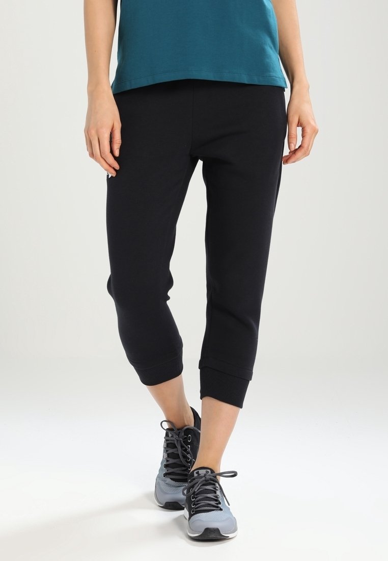 Svarta capri-byxor i sweatpantsmodell med ribbade muddar, tillsammans med grå träningsskor. Tyget verkar mjukt och stretchy, passar bra för avslappnad användning.