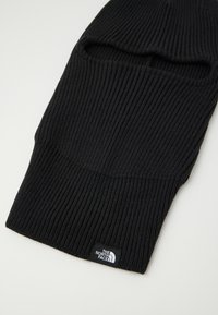 Melna adīta balaklava ar vertikāliem ribojumiem, ar izgriezumiem acīm un logotipa uzšuvi no The North Face. Mīksta tekstūra.