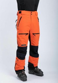 Oranssi ja musta hiihtohousut, joissa on säädettävät hihnat, vetoketjulliset taskut ja vahvistettu alaosa. Valmistettu kestävästä, säänkestävästä materiaalista.