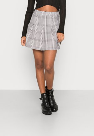 Safaio mini em xadrez preto e branco, plissada, com uma cintura elástica, combinada com botas de tornozelo pretas com fivelas e fechos de zíper.