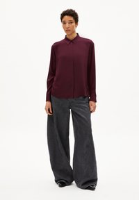 Burgundy long-sleeve shirt with a pointed collar, paired with oversized gray denim pants featuring prominent seams and a wide leg.