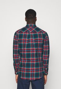 Camisa de cuadros de manga larga en azul marino, rojo y verde. Presenta un patrón de cuadros tradicional, puños con botones y un dobladillo curvado.