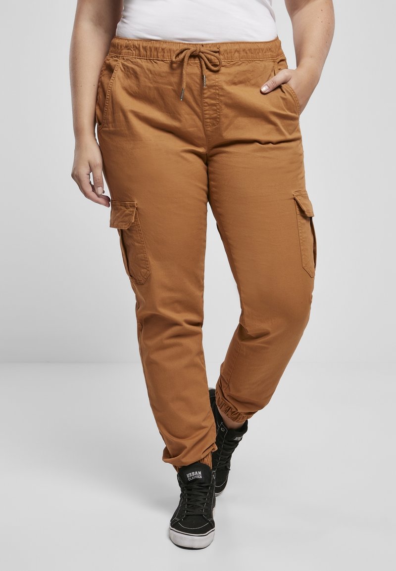Personne portant un pantalon cargo marron avec des bas élastiques et une taille à cordon, associé à des baskets montantes noires et un haut blanc.