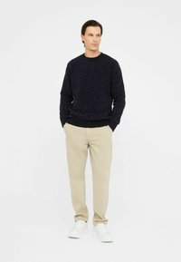 Maglione blu navy a maglia con un motivo testurizzato, abbinato a pantaloni beige chiaro e sneakers bianche. Design semplice e dal taglio rilassato.