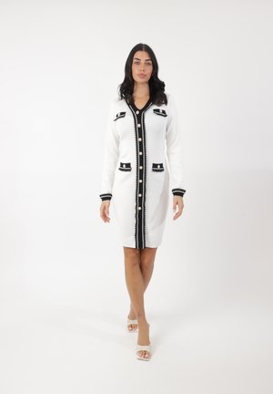 Vestido de punto blanco con acentos negros, con un escote en V, ribete estampado, cierres de botones y bolsillos. Tejido texturizado y corte ajustado.