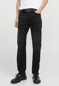 Jeans in denim nero con vestibilità a gamba dritta, texture sottile, cinque tasche e cintura con fibbia argentata. Indossati con scarpe nere stringate.