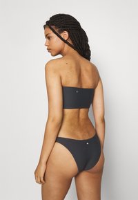 Melna ribota bandeau bikini augšdaļa un atbilstošas augstas vidukļa apakšdaļa. Abiem gabaliem ir smalks aksesuārs. Gluda, elastīga auduma.