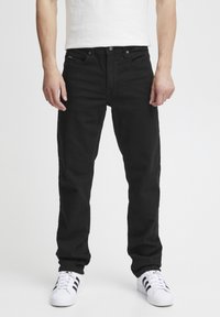 Black denim jeans with a straight cut, five-pocket design, and a button closure. Worn with white athletic shoes featuring black stripes.