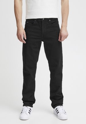 Black denim jeans with a straight cut, five-pocket design, and a button closure. Worn with white athletic shoes featuring black stripes.