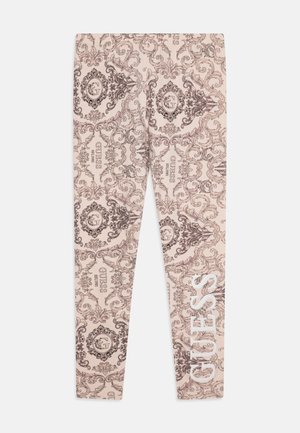 Leggings beige con un intricato motivo barocco marrone, con il nome del marchio "GUESS" in bianco sul lato.
