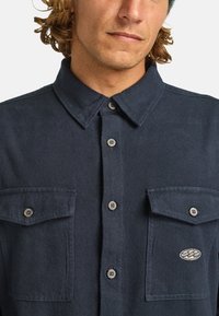 Donkerblauw overhemd met knopen, gemaakt van textuurstof, met een puntige kraag, twee klepzakken en geborduurd logo op de linkerpocket.